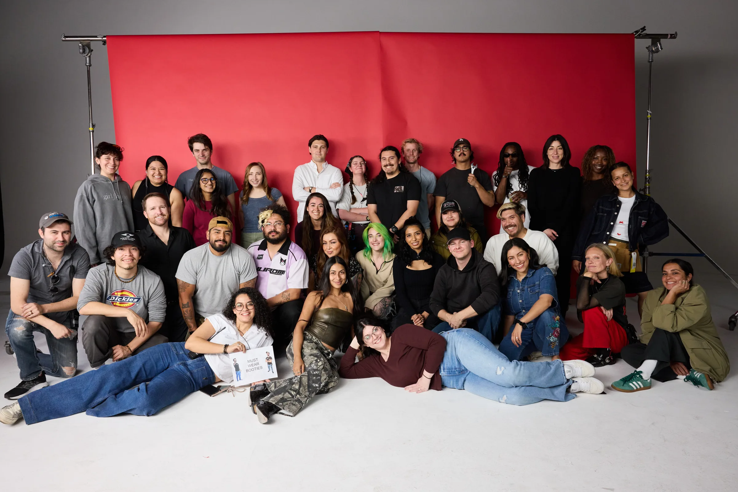 Full crew photo — approximately 30 people against red backdrop, showing the scale of the production
