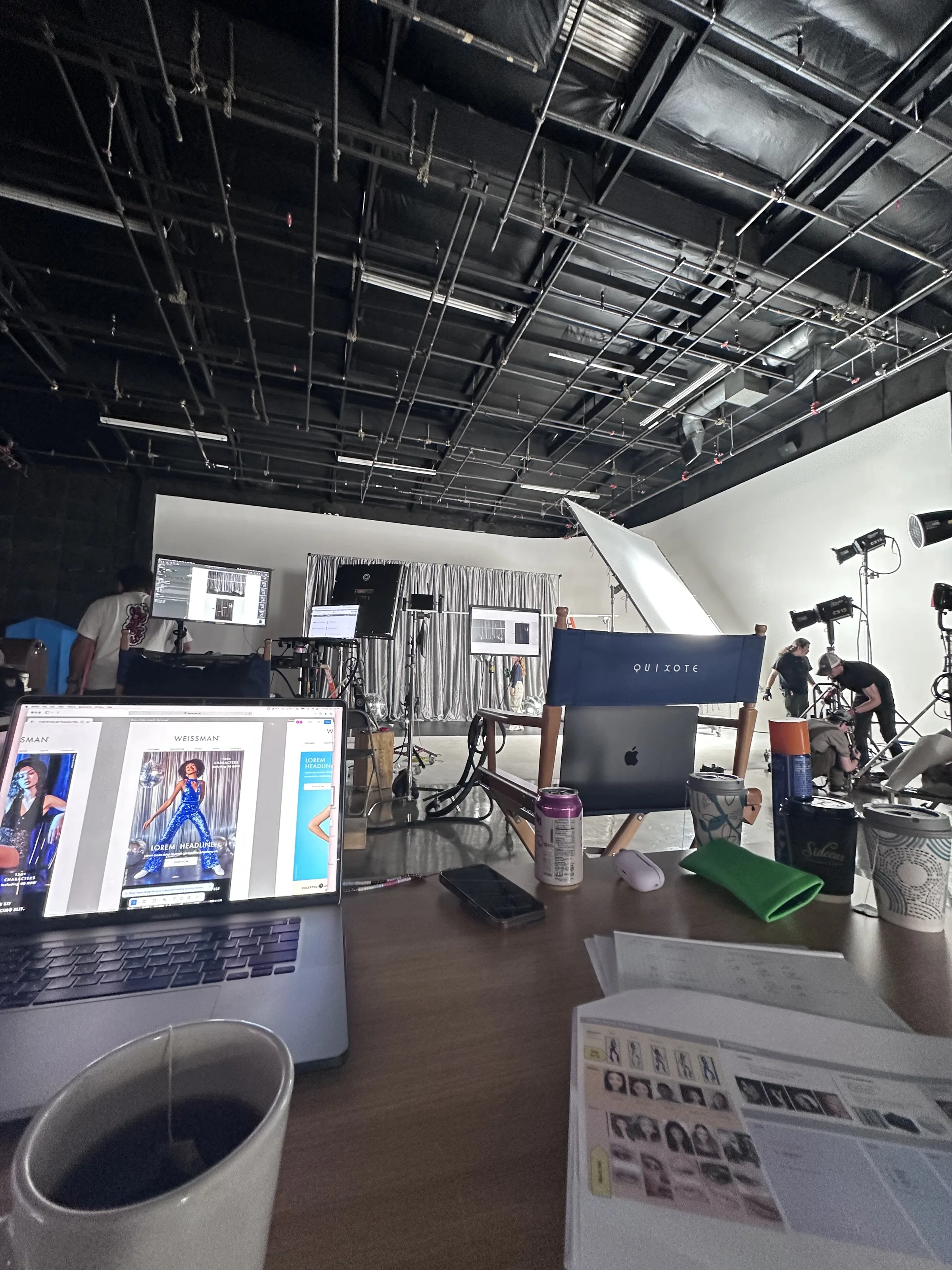 Laptop showing website layouts with printed shot sheet on desk, Quixote director's chair, set in background