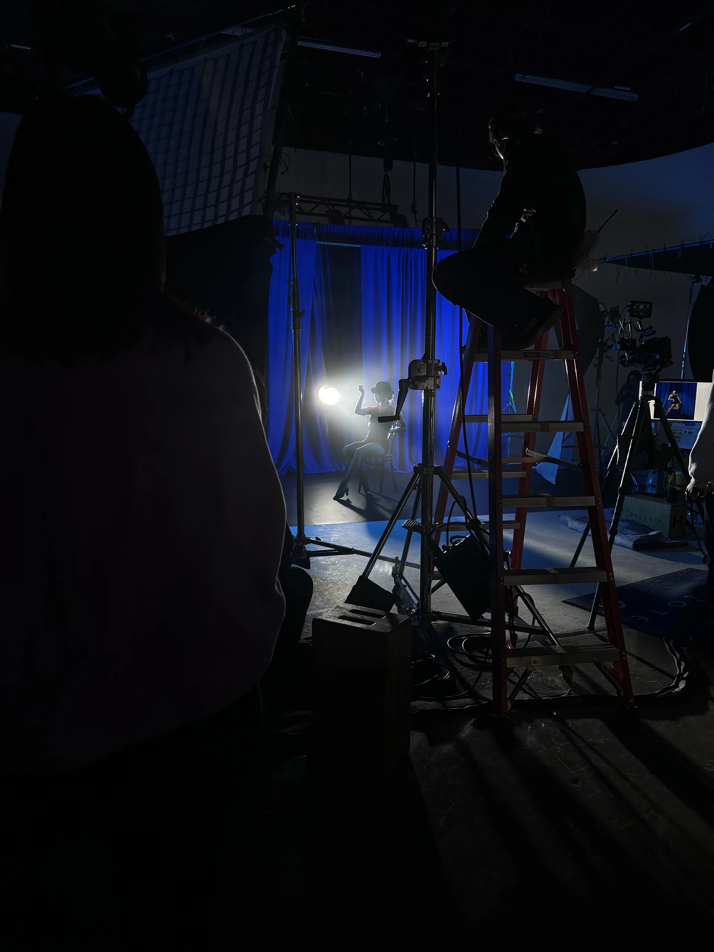 Cabaret dancer with bowler hat and fishnets against blue drape and haze — behind the scenes of the final Cabaret banner