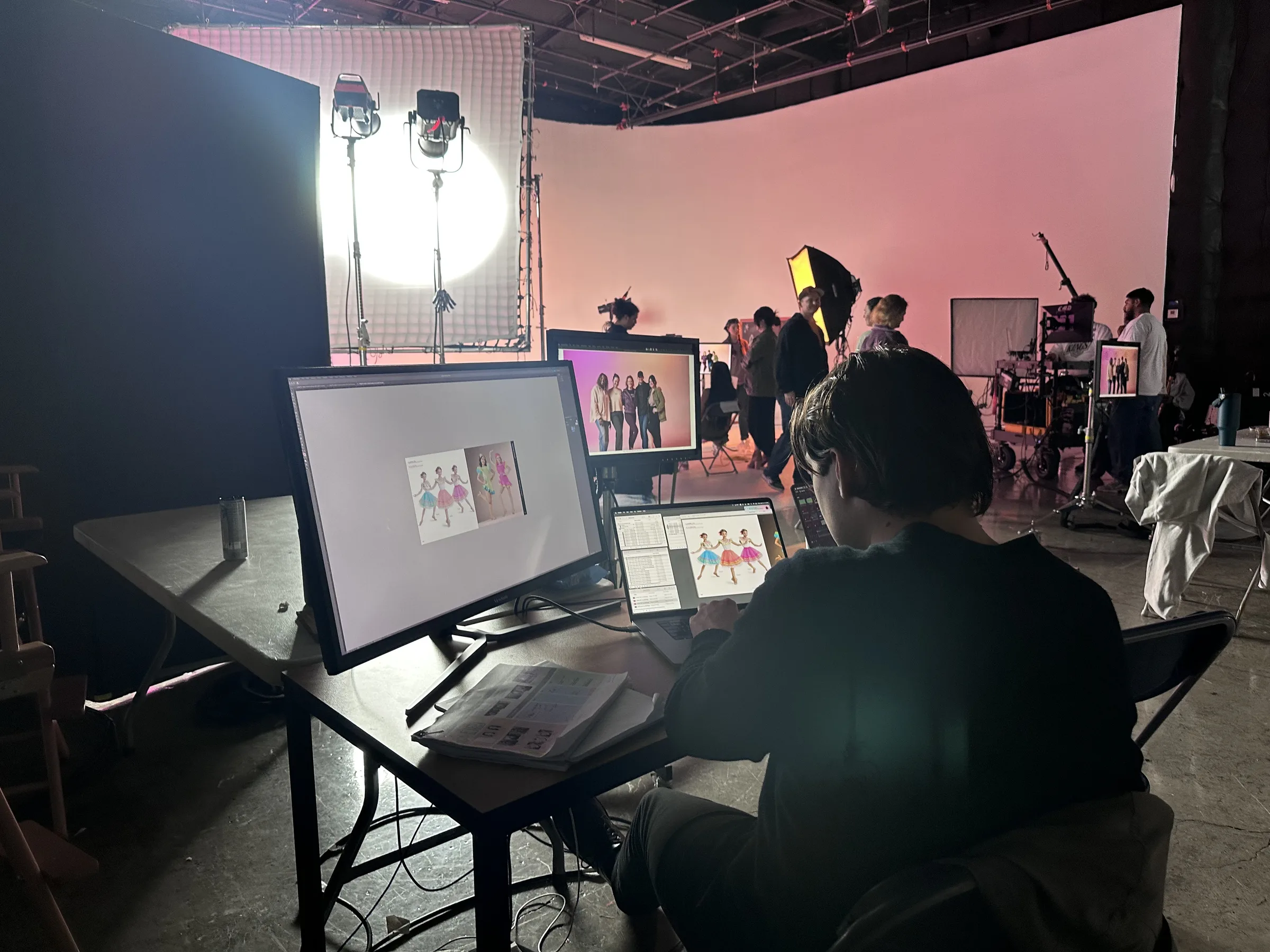 Production artist from behind at multi-screen workstation, pink cyclorama wall glowing in background