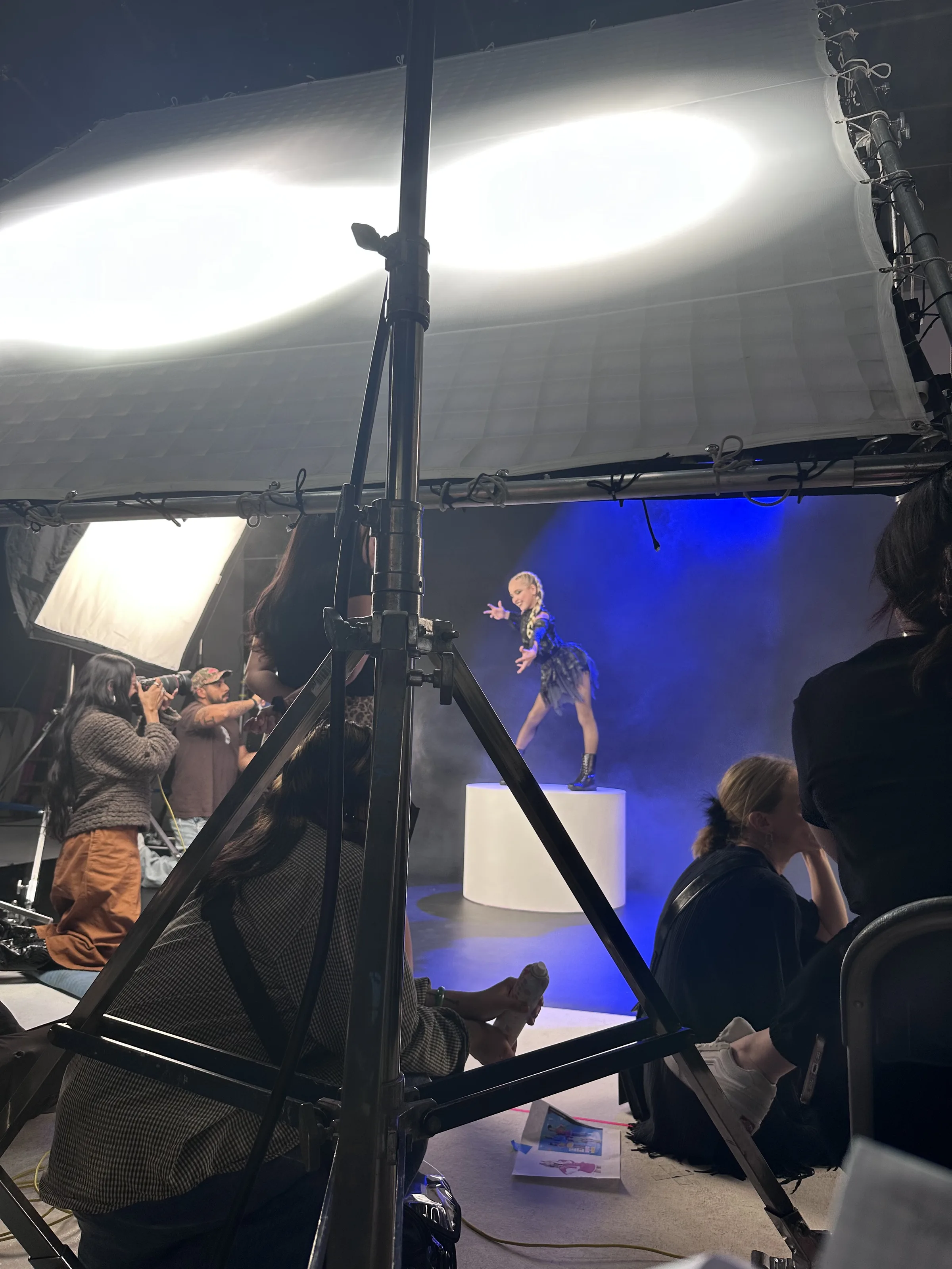 Roaring 20s dark set — dancer on white pedestal with blue haze, crew visible, most cinematic BTS shot